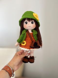 a small doll is being held up by a woman in a green hat and dress