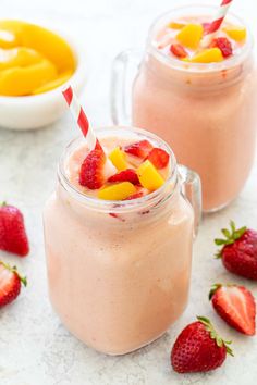 two mason jars filled with fruit smoothies and topped with strawberries, peaches, and mango slices