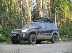 an suv parked on the side of a dirt road in front of trees and rocks