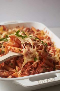 a white casserole dish filled with pasta and meat topped with parmesan cheese