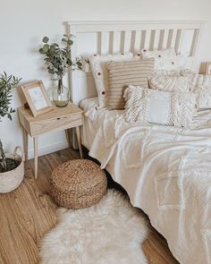 a bedroom with white bedding, pillows and plants on the side table in front of the bed