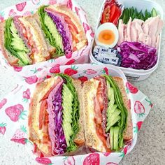 two sandwiches with lettuce, tomato, and other foods in containers on a table