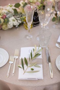 the table is set with silverware, napkins, and greenery on it