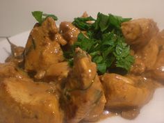 a white plate topped with meat covered in gravy and garnished with parsley