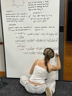 a woman sitting on the floor in front of a whiteboard with calculations written on it