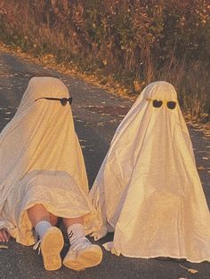 two people dressed in white sitting on the side of a road next to each other