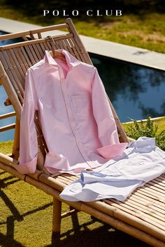 a pink shirt sitting on top of a wooden bench next to a pool and water