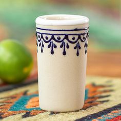 a white coffee cup sitting on top of a rug next to an orange and green apple