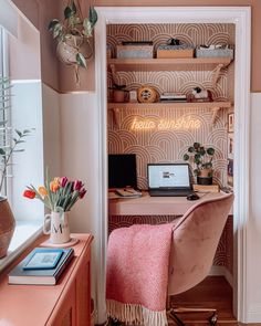 a desk with a laptop on top of it next to a shelf filled with flowers