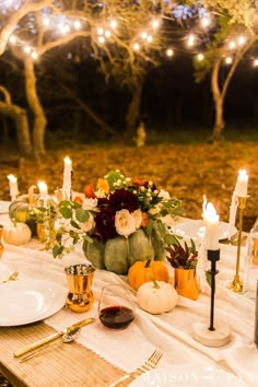 a table with candles, plates and pumpkins on it is set for an outdoor dinner