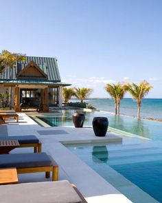 an outdoor swimming pool with lounge chairs next to it and the ocean in the background