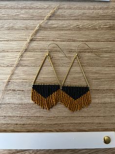 two tone beaded earrings with gold and black accents on a wooden table next to a pair of scissors