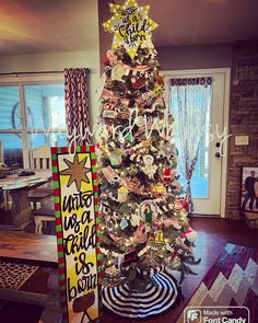 a decorated christmas tree in the middle of a living room next to a sign that says,