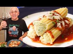 an older man holding a glass of wine next to a plate of pasta and sauce