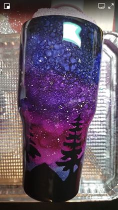 a purple and black cup sitting on top of a plastic container with trees painted on it