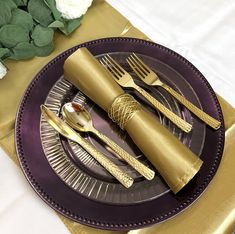 a purple plate topped with gold colored utensils next to a white and green flower