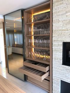 an open cabinet with wine glasses on it in front of a brick wall and fireplace