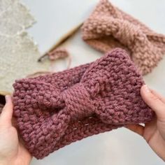 a person holding up a knitted bow on top of a piece of cloth next to other items