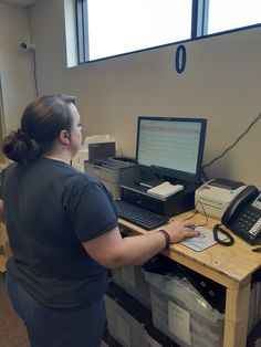 a woman standing in front of a desk with a computer and printer on it