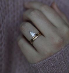 a woman's hand wearing a gold ring with a white diamond on the middle