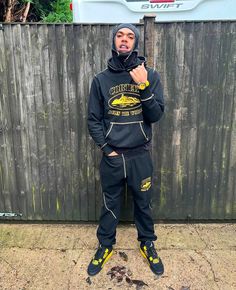 a man standing in front of a wooden fence wearing a hoodie and sweatpants