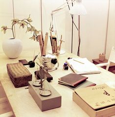 an office desk with books, pens and notebooks on it next to a lamp