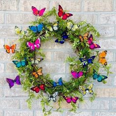 a wreath made out of green plants and colorful butterflies on a brick wall behind it