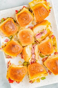 a white plate topped with mini sandwiches covered in cheese and ham on top of lettuce