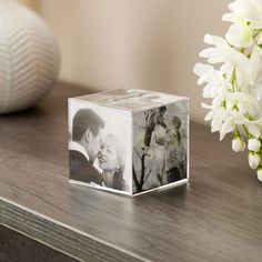 a photo cube sitting on top of a wooden table next to a vase with flowers