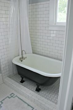 an old fashioned bathtub in a bathroom with white tile walls and flooring, along with a black claw foot tub