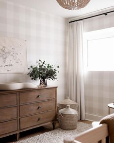 a room with a dresser, chair and plant in it's centerpiece next to a window