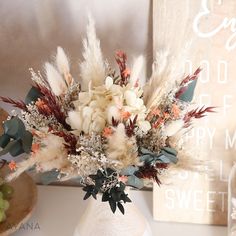 a white vase filled with lots of flowers on top of a table next to a sign