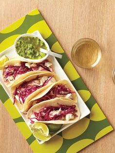 three tacos with red cabbage and guacamole on a green and yellow plate