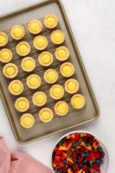 a pan filled with mini pies next to a bowl of fruit