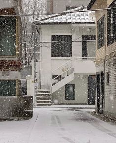 an alley way with snow falling on the ground and stairs leading up to two buildings