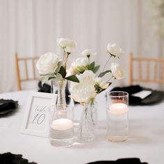 two vases filled with white flowers sitting on top of a table next to candles