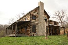 an old log cabin sitting on top of a lush green field