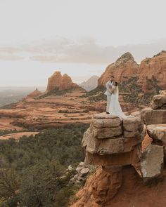 a bride and groom standing on top of a rock formation