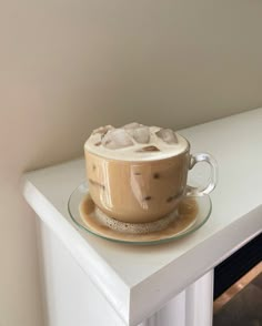 a cup of hot chocolate with whipped cream on the top sits on a glass saucer