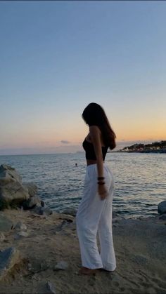 a woman standing on top of a sandy beach next to the ocean at sunset or dawn