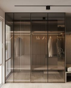 a walk in closet with glass doors and clothes hanging on the wall next to it