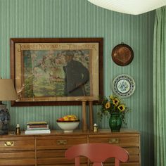 a painting hangs on the wall next to a dresser with a bowl of fruit in front of it