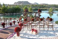 an outdoor wedding set up with chairs and flowers on the ground next to a lake