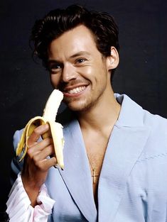 a man holding a banana in his right hand and smiling at the camera while wearing a blue suit