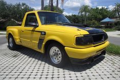 a yellow pick up truck parked in front of a palm tree lined driveway with white and black stripes on the hood