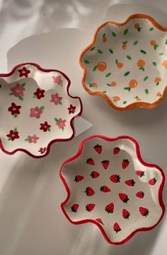 three plates with designs on them sitting on a white tableclothed surface, one has strawberries and the other has oranges