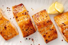 four pieces of salmon on a white plate with lemon wedges and seasoning next to it