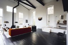 a living room with white walls and black flooring is furnished with modern furniture, including a red couch