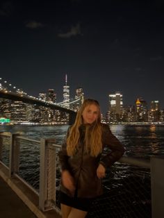 a woman standing on the side of a bridge next to a body of water at night