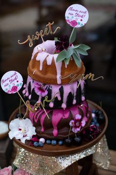 a three tiered cake decorated with pink and black icing, topped with flowers